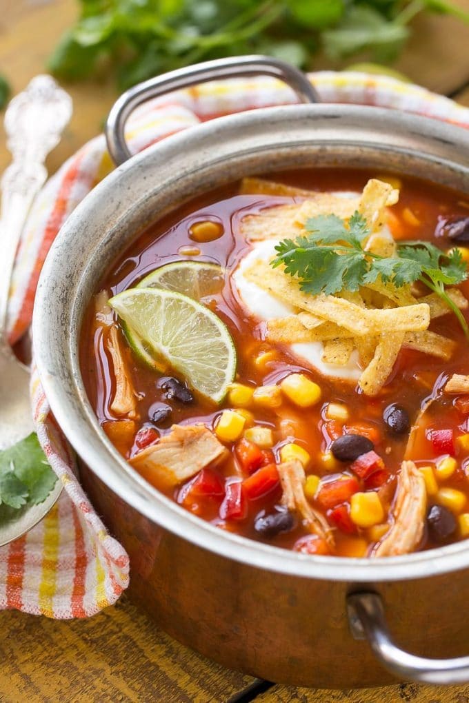 A pot of chicken taco soup with sour cream, tortilla strips and lime wedges as toppings.