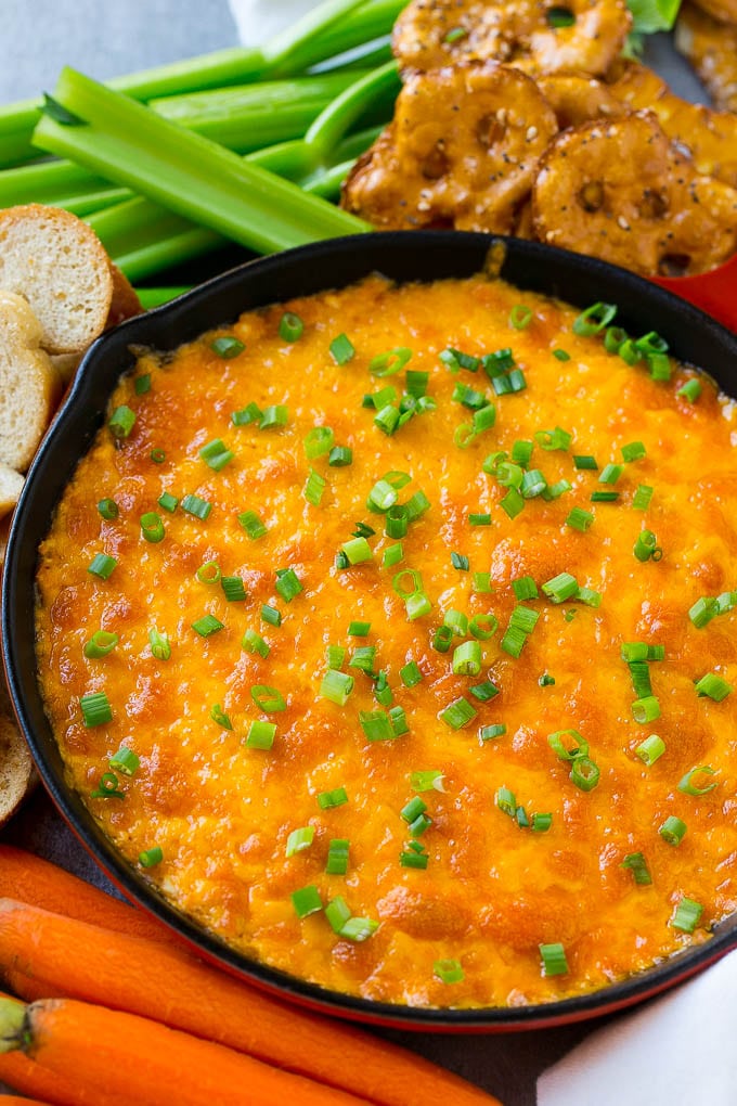 Buffalo Ranch Chicken Dip | Buffalo Chicken Dip | Baked Buffalo Dip | Cheesy Buffalo Dip #buffalowings #buffalochicken #dip #lowcarb #appetizer #sadud Buffalo ranch chicken dip topped with melted cheese and green onions, surrounded by vegetables, pretzels and baguette slices.