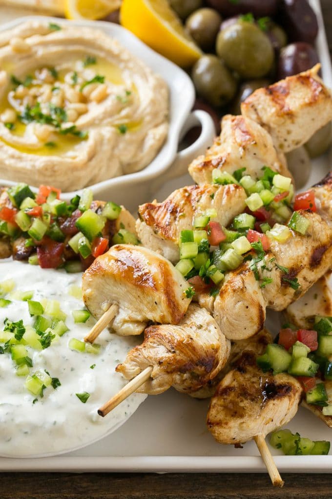 Greek Chicken Souvlaki Recipe | Easy Greek Chicken | Chicken Souvlaki | Greek Chicken Skewers | Easy Greek Chicken Skewers #chicken #kabobs #glutenfree #keto #lowcarb #grilling #sadud A tray of chicken souvlaki kabobs with olives, hummus, pita bread and yogurt sauce.