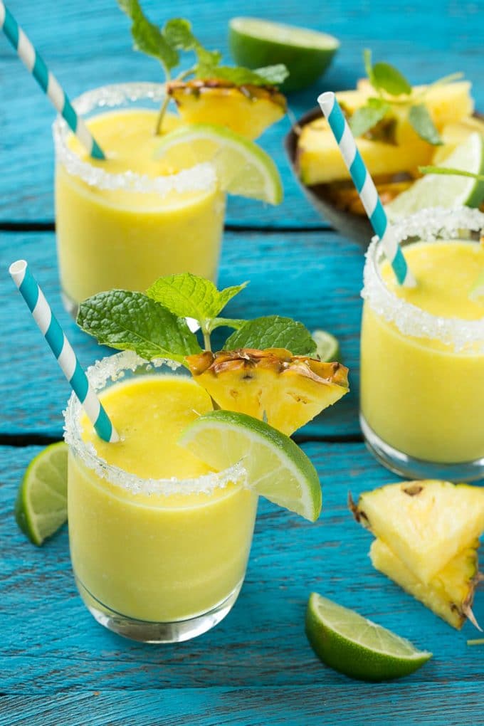 Pineapple Coconut Smoothie Recipe |Tropical Smoothie | Pineapple Smoothie #smoothie #pineapple #coconut #healthy #cleaneating #sadud Glasses of pineapple coconut smoothie garnished with limes and mint.