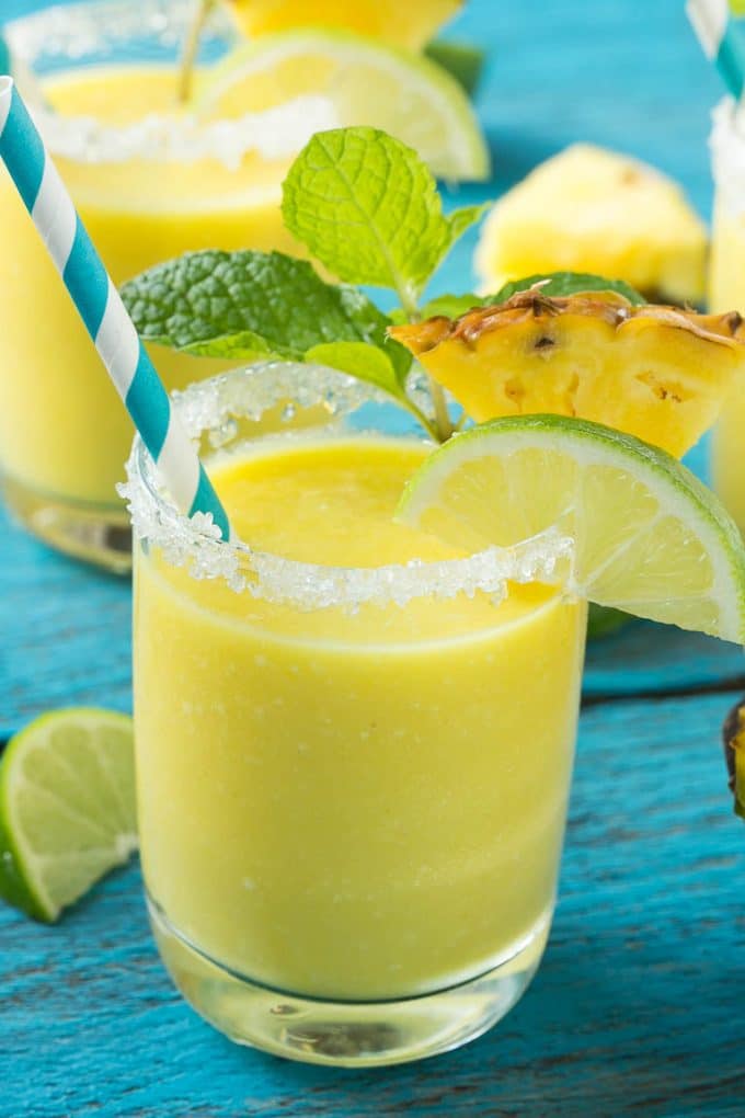 Pineapple Coconut Smoothie Recipe |Tropical Smoothie | Pineapple Smoothie #smoothie #pineapple #coconut #healthy #cleaneating #sadud A cup of pineapple smoothie with garnishes of lime, pineapple wedges and mint sprigs.