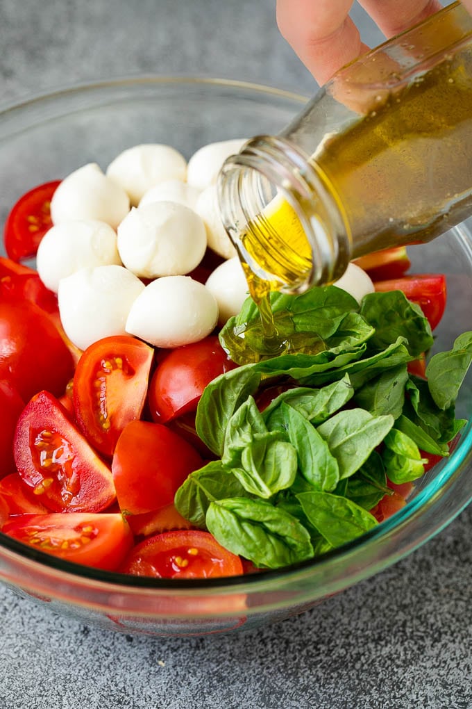 Caprese Salad Recipe | Tomato Salad #salad #tomato #mozzarella #cheese #basil #caprese #summer #sadud Olive oil being poured over tomatoes, mozzarella and basil leaves.