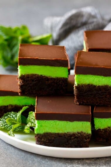Layered mint brownies with frosting on a serving plate, garnished with fresh mint.