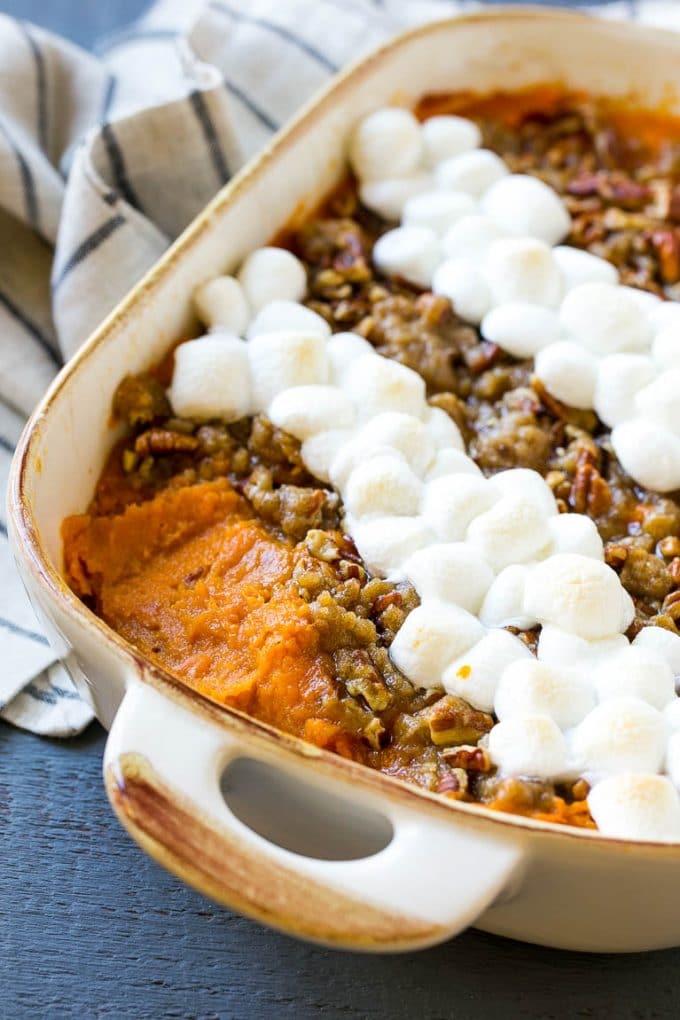 This recipe for sweet potato casserole with marshmallows is mashed spiced sweet potatoes, topped with both a pecan streusel topping and plenty of mini marshmallows. A holiday classic that's a family favorite! A yams dish with pecan streusel, with a spoonful removed.