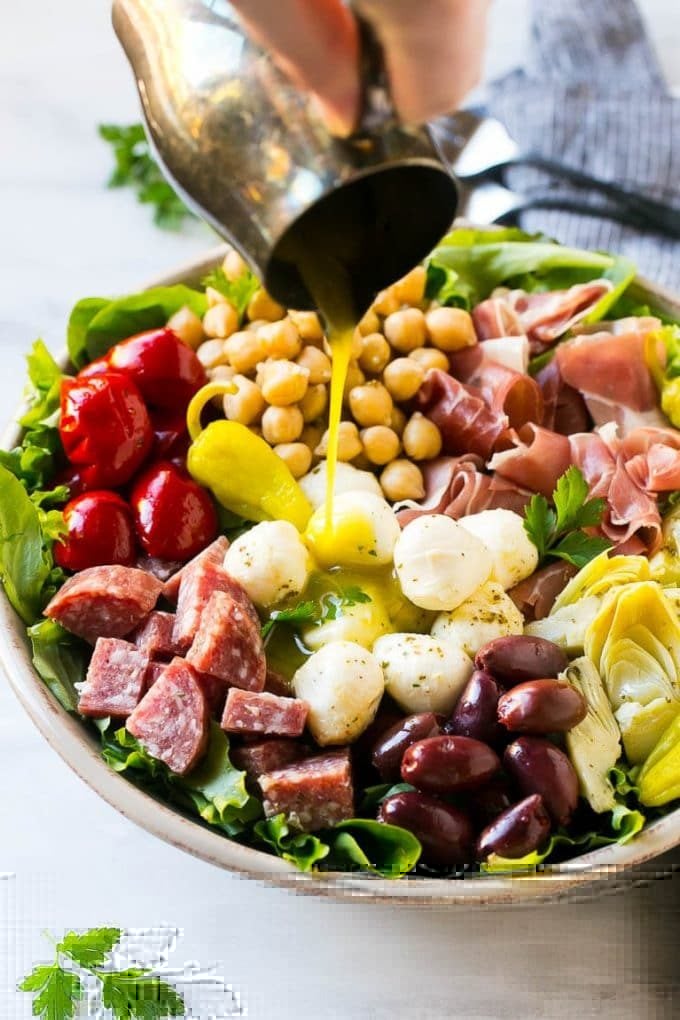 Antipasto Salad Recipe | Italian Salad | Main Course Salad | Antipasto Recipe #salad #salami #italianfood #dinner #lunch #sadud A pitcher of dressing being poured over antipasto salad.