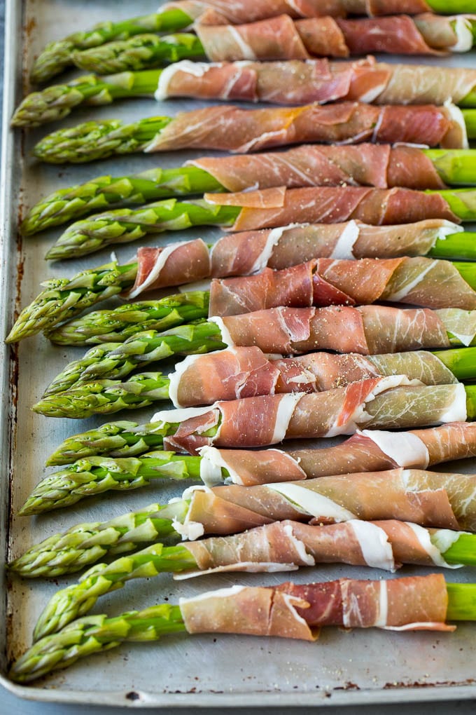 This prosciutto wrapped asparagus is fresh asparagus stalks flavored with savory prosciutto, then broiled to crispy perfection. Asparagus on a sheet pan with prosciutto, ready for the oven.