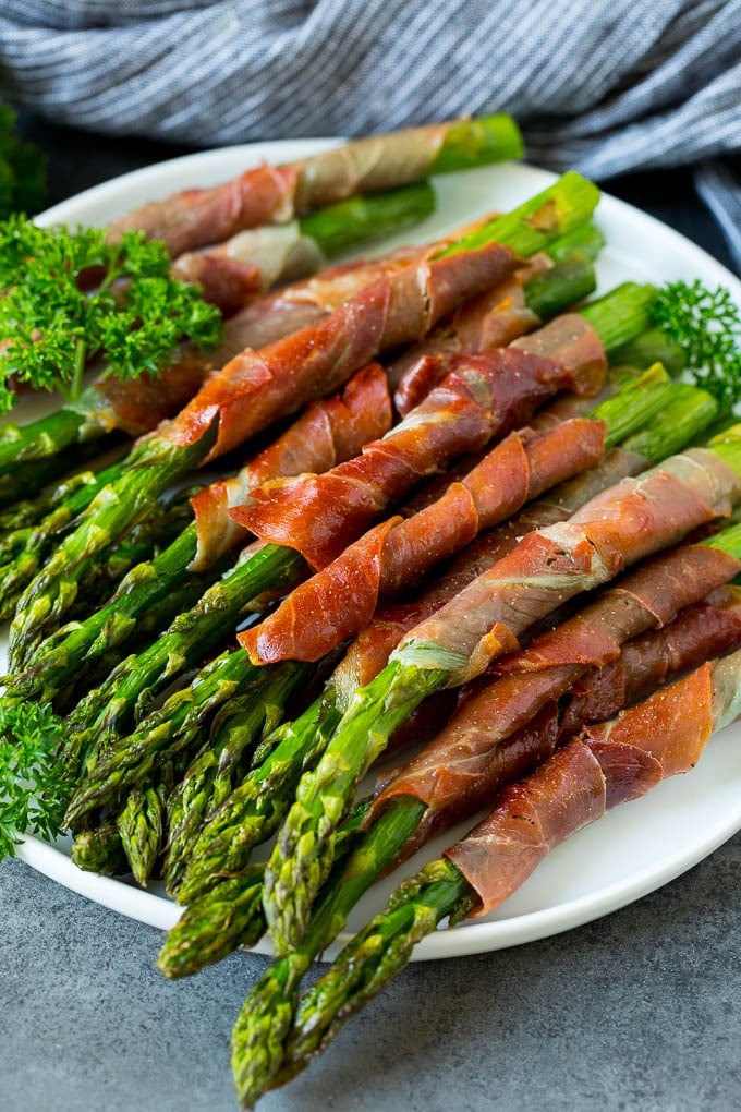 This prosciutto wrapped asparagus is fresh asparagus stalks flavored with savory prosciutto, then broiled to crispy perfection. A plate of prosciutto wrapped asparagus garnished with fresh parsley.