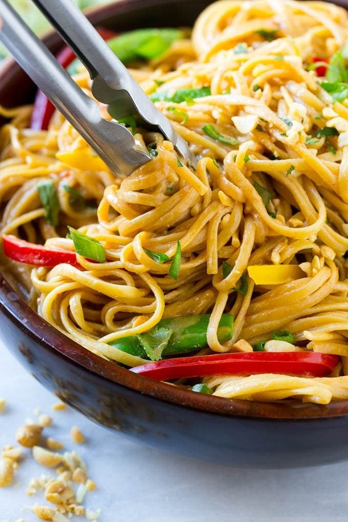 Tongs serving up a portion of Thai peanut noodles.