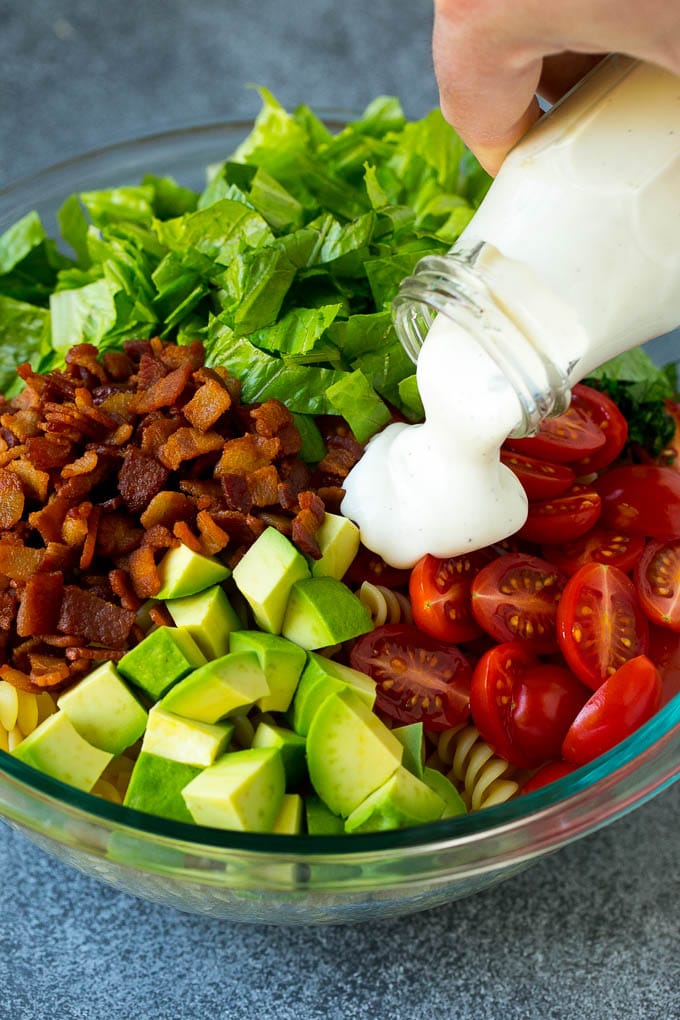 BLT Pasta Salad Recipe | Easy Pasta Salad | Bacon Pasta Salad #salad #pasta #blt #bacon #avocado #dinner #sadud Ranch dressing being poured over tomatoes, lettuce, bacon and avocado.