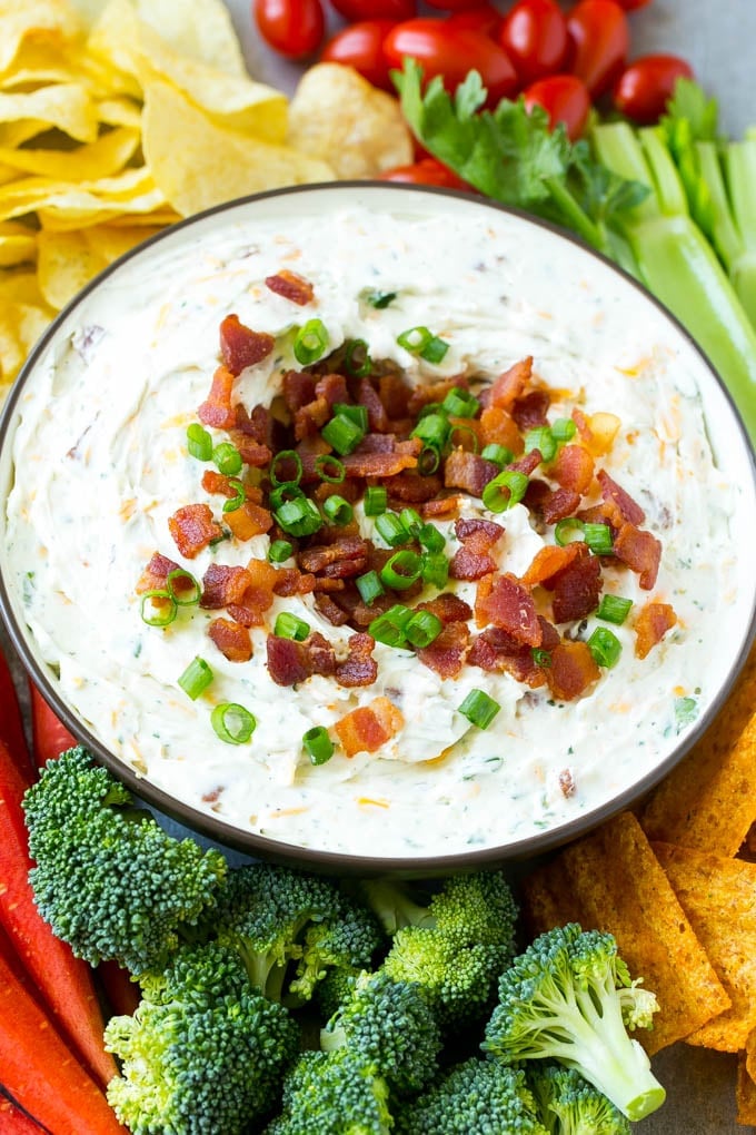 Bacon Ranch Dip Recipe | Homemade Ranch Dip | Easy Dip Recipe | Cheddar Ranch Dip #ranch #ranchdip #bacondip #dip #snack #sadud #baconranchdip A bowl of creamy bacon cheddar ranch dip surrounded by vegetables and chips.