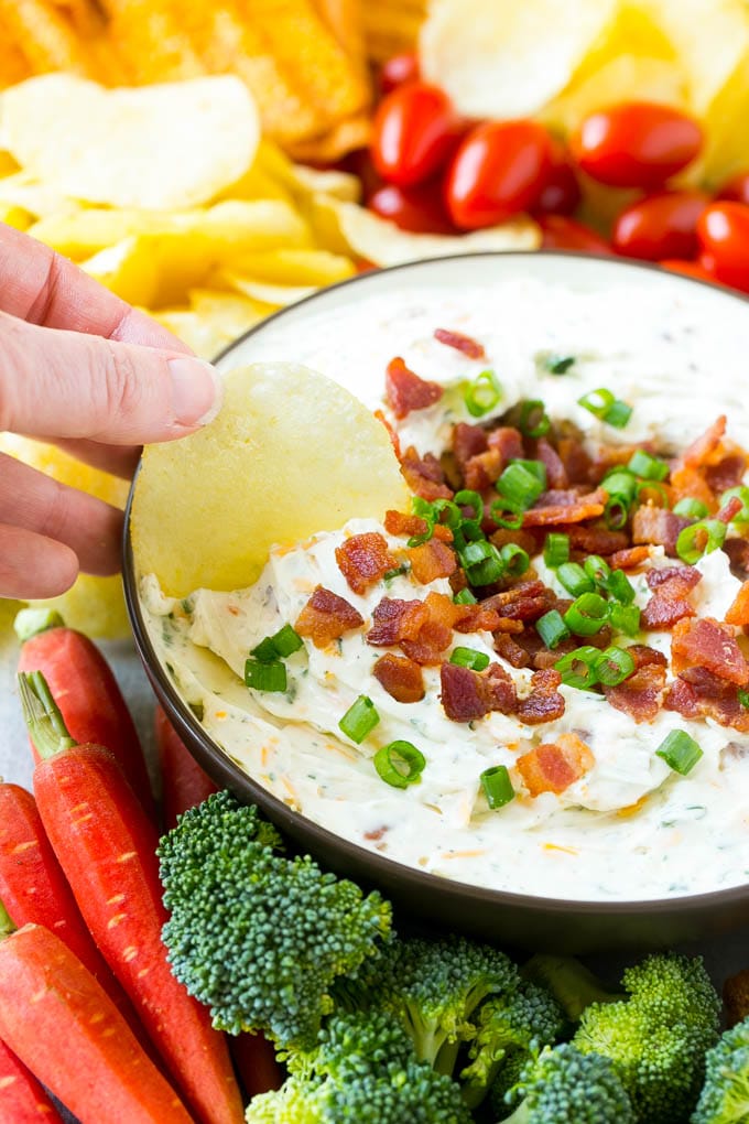 Bacon Ranch Dip Recipe | Homemade Ranch Dip | Easy Dip Recipe | Cheddar Ranch Dip #ranch #ranchdip #bacondip #dip #snack #sadud #baconranchdip A hand scooping up bacon ranch dip with a potato chip.