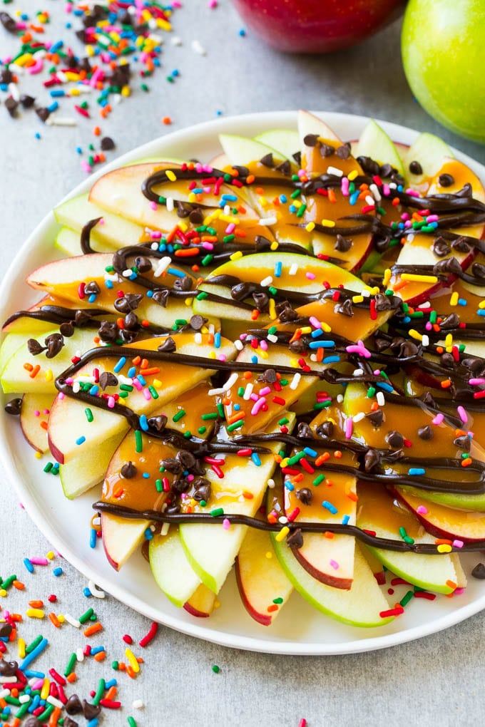 Apple Nachos Recipe | After School Snack | Caramel Apples #apple #apples #caramelapple #snack #dessert #sadud A plate of sliced apple nachos topped with caramel and chocolate sauces, rainbow sprinkles and mini chocolate chips
