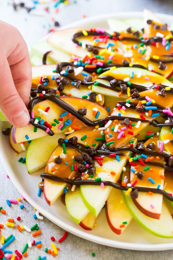 Apple Nachos Recipe | After School Snack | Caramel Apples #apple #apples #caramelapple #snack #dessert #sadud A plate of caramel apple nachos with a hand reaching out to take one.