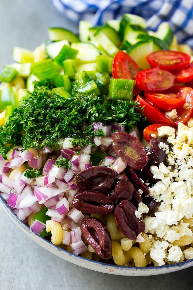 Greek Pasta Salad | Easy Pasta Salad | Vegetable Pasta Salad #pasta #salad #greek #cucumber #tomato #vegetarian #dinner #sadud A bowl of pasta with red onion, kalamata olives, bell pepper and tomatoes, with a drizzle of Greek dressing.