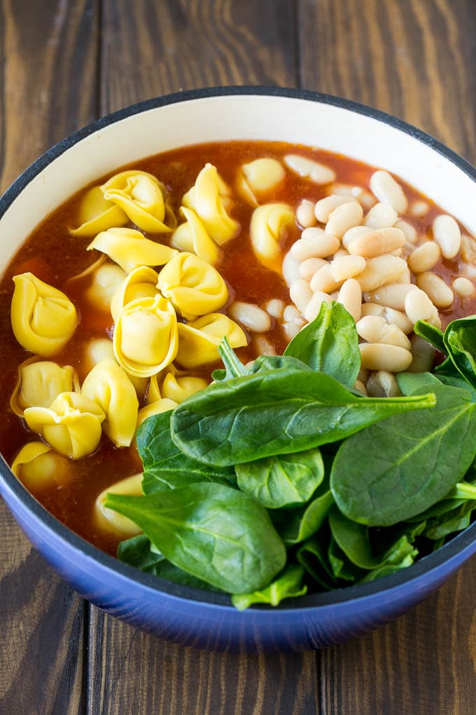 Tortellini Soup Recipe | Sausage Soup | Italian Soup #soup #sausage #pasta #tortellini #dinner #sadud A pot with ingredients like spinach leaves and white beans.