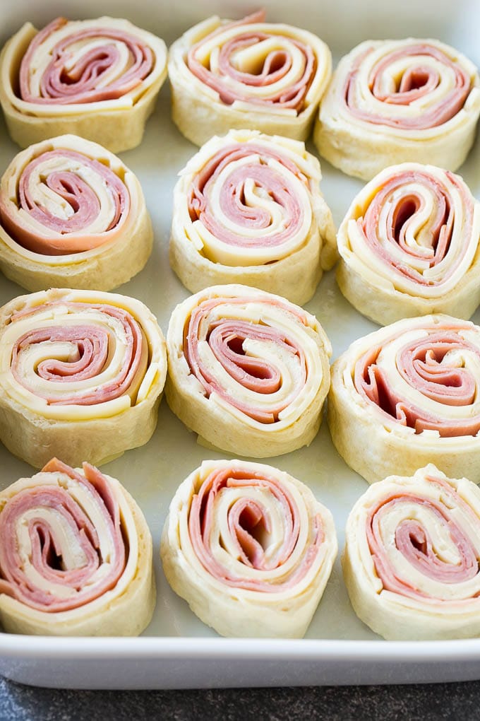 Ham and Cheese Pinwheels Recipe | Ham and Cheese Roll Ups | Ham and Cheese Rolls | Ham and Cheese Bread Rolls #ham #cheese #appetizer #pinwheels #sadud Rolled up ham, cheese and pizza dough circles in a baking dish.