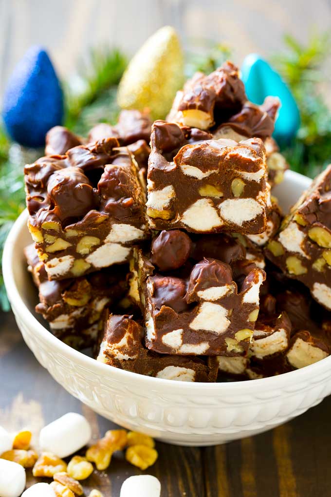 Rocky Road Fudge | Chocolate Marshmallow Fudge | Chocolate Nut Fudge | Microwave Fudge #fudge #chocolatefudge #nobake #chocolate #dessert #rockyroad #sadud A bowl of fudge squares with holiday decorations in the background.