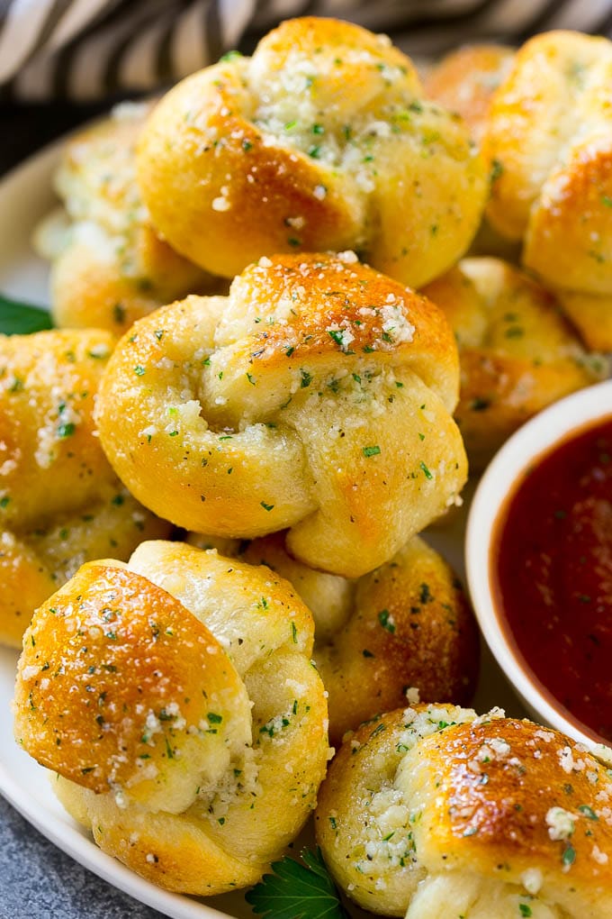Garlic Knots Recipe | Garlic Rolls | Garlic Butter Rolls | Garlic Bread Recipe #garlic #garlicbread #garlicknots #breadsticks #sadud A plate of garlic knots slathered in butter next to a cup of marinara sauce.