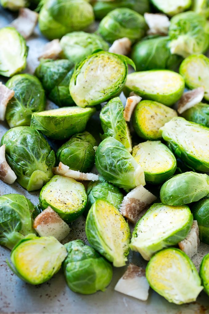 \These bacon roasted brussels sprouts are crispy on the outside, soft on the inside and full of smoky flavor. Raw halved brussels sprouts with uncooked bacon on a sheet pan.