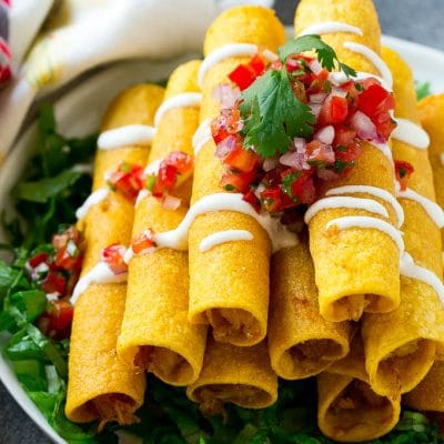 A stack of chicken taquitos with a drizzle of sour cream and pico de gallo topping.