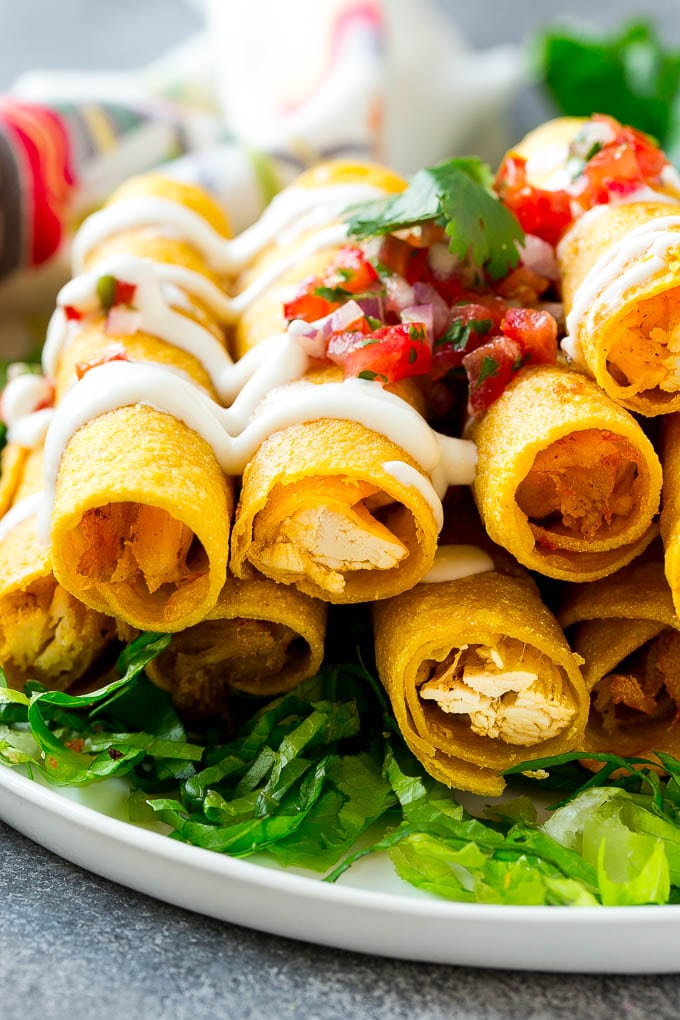 Chicken Taquitos Recipe | Baked Chicken Taquitos | Fried Chicken Taquitos | Mexican Appetizer | Chicken Tortillas #taquitos #chicken #appetizer #tortillas #mexicanfood #sadud A plate of chicken taquitos on a bed of lettuce, topped with sour cream and pico de gallo.