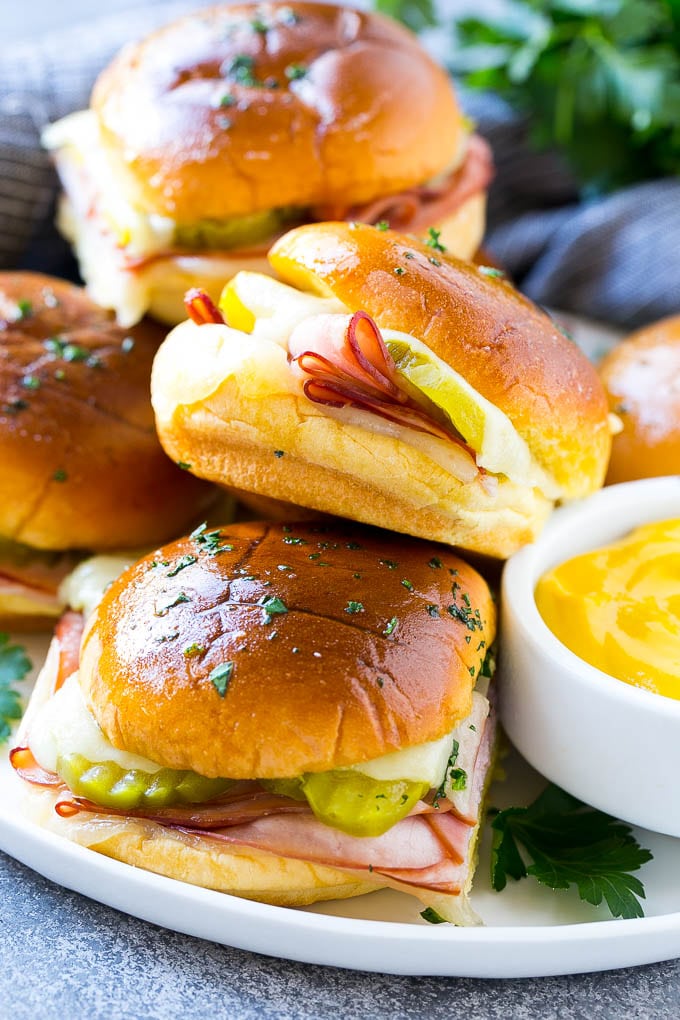 Cuban Sliders Recipe | Cuban Sandwich Recipe | Slider Sandwiches | Ham and Cheese Sliders #sliders #sandwiches #ham #cheese #appetizer #sadud A plate full of Cuban sliders with cheese, pickles and ham on buns.