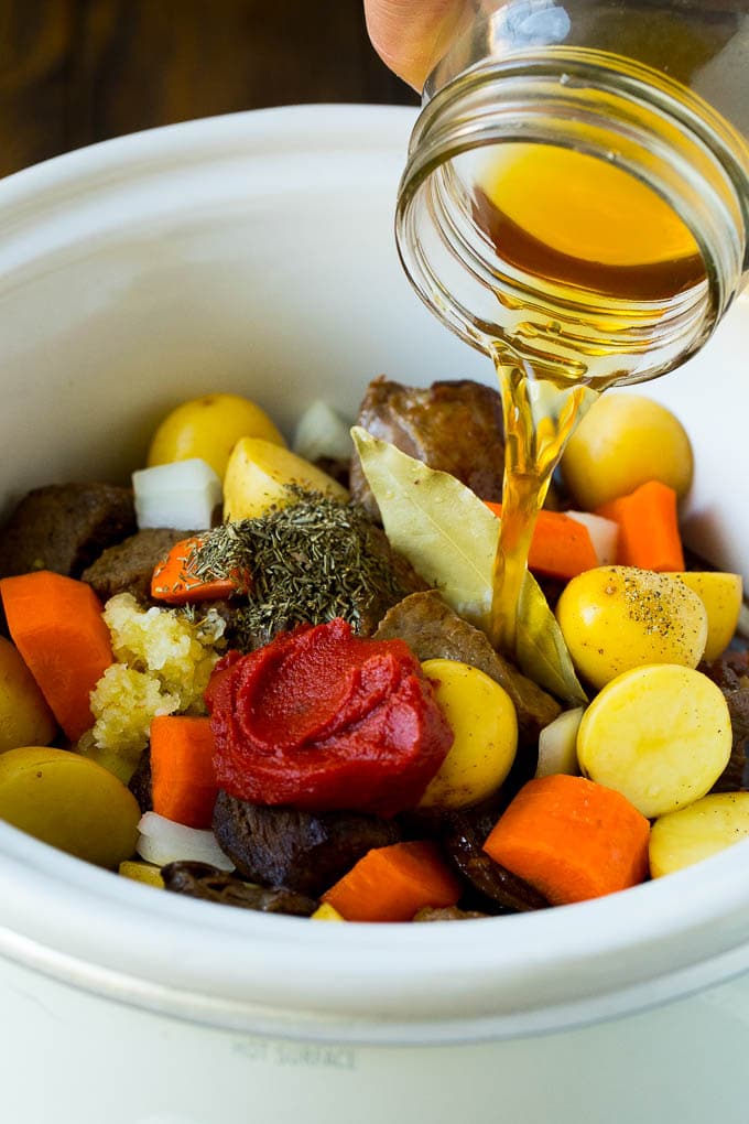 Slow Cooker Beef Stew Recipe | Crockpot Beef Stew #stew #soup #beef #slowcooker #crockpot #dinner #sadud Broth being poured into a slow cooker filled with beef and vegetables.