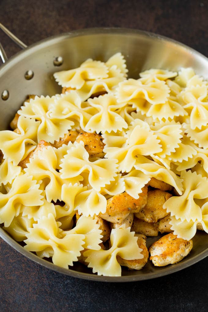 This chicken pesto pasta is sauteed chicken, farfalle pasta and cherry tomatoes, all tossed in basil pesto and finished off with parmesan cheese. Chicken and farfalle pasta in a pan.