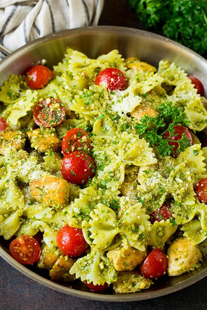 This chicken pesto pasta is sauteed chicken, farfalle pasta and cherry tomatoes, all tossed in basil pesto and finished off with parmesan cheese. Chicken pesto pasta in a pan with cherry tomatoes and parmesan cheese.