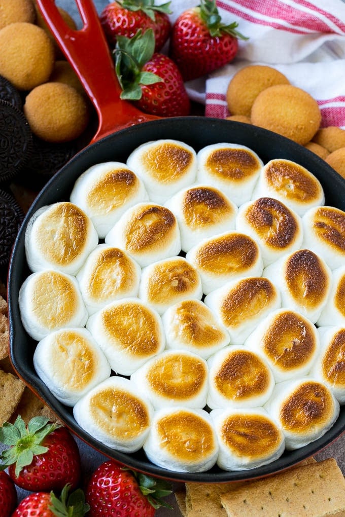 S'mores Dip Recipe | S'mores Skillet | Baked S'mores #smores #dip #chocolate #marshmallow #dessert #sadud A skillet of s'mores dip with melted chocolate chips and toasted marshmallows, surrounded by graham crackers, cookies and strawberries.