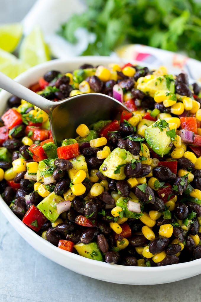 Black Bean and Corn Salad Recipe | Mexican Salad | Black Bean Salad | Bean Salad #salad #beans #corn #mexicanfood #sadud A bowl of black bean and corn salad with a serving spoon in it.