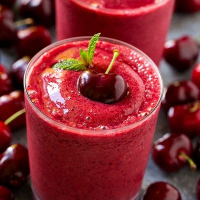 A cherry smoothie garnished with a fresh dark cherry and mint.