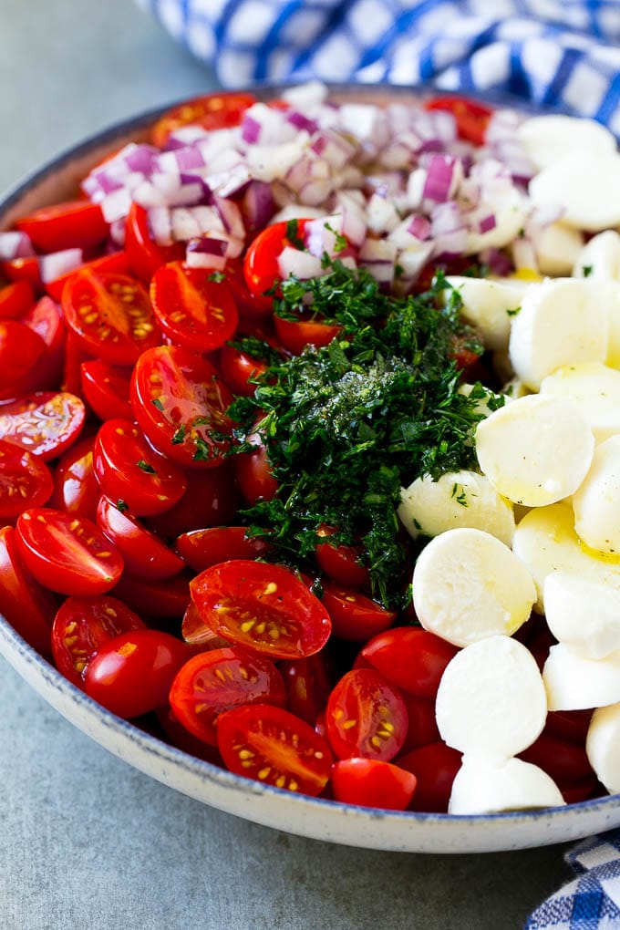Cherry Tomato Salad Recipe | Tomato Mozzarella Salad | Caprese Salad | Tomato Salad #tomatoes #salad #tomatosalad #caprese #sadud Cherry tomatoes, herbs, mozzarella balls and red onion drizzled with dressing in a bowl.
