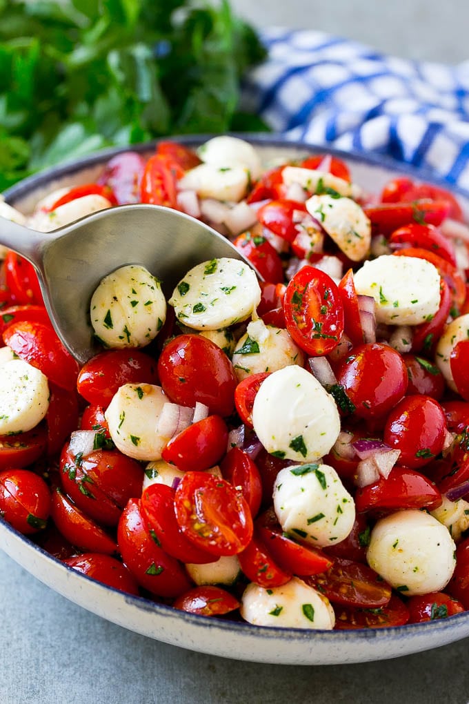 Cherry Tomato Salad Recipe | Tomato Mozzarella Salad | Caprese Salad | Tomato Salad #tomatoes #salad #tomatosalad #caprese #sadud A bowl of cherry tomato salad with a serving spoon in it.