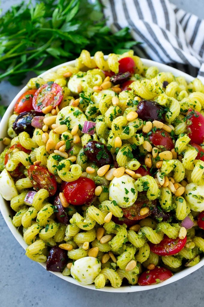 Pesto Pasta Salad | Italian Pasta Salad | Easy Pasta Salad #pasta #salad #pesto #olives #tomatoes #sadud A bowl of pesto pasta salad topped with pine nuts and chopped parsley.