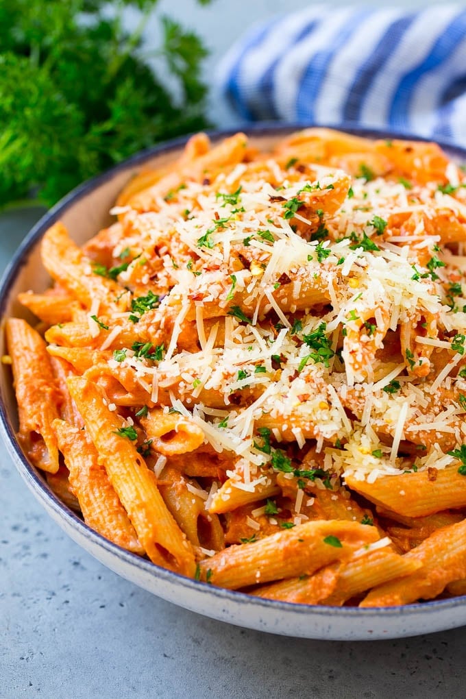 This Penne alla Vodka is tender penne pasta tossed in a rich and delicious tomato, vodka and cream sauce. Add a sprinkling of parmesan cheese and you'll have a restaurant quality meal in the comfort of your own home. A bowl of penne alla vodka pasta topped with parmesan cheese, parsley and red pepper flakes.
