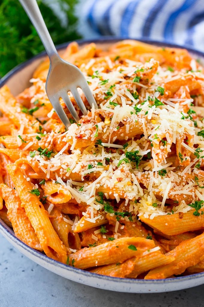 This Penne alla Vodka is tender penne pasta tossed in a rich and delicious tomato, vodka and cream sauce. Add a sprinkling of parmesan cheese and you'll have a restaurant quality meal in the comfort of your own home. A bowl of penne alla vodka with a fork in it.