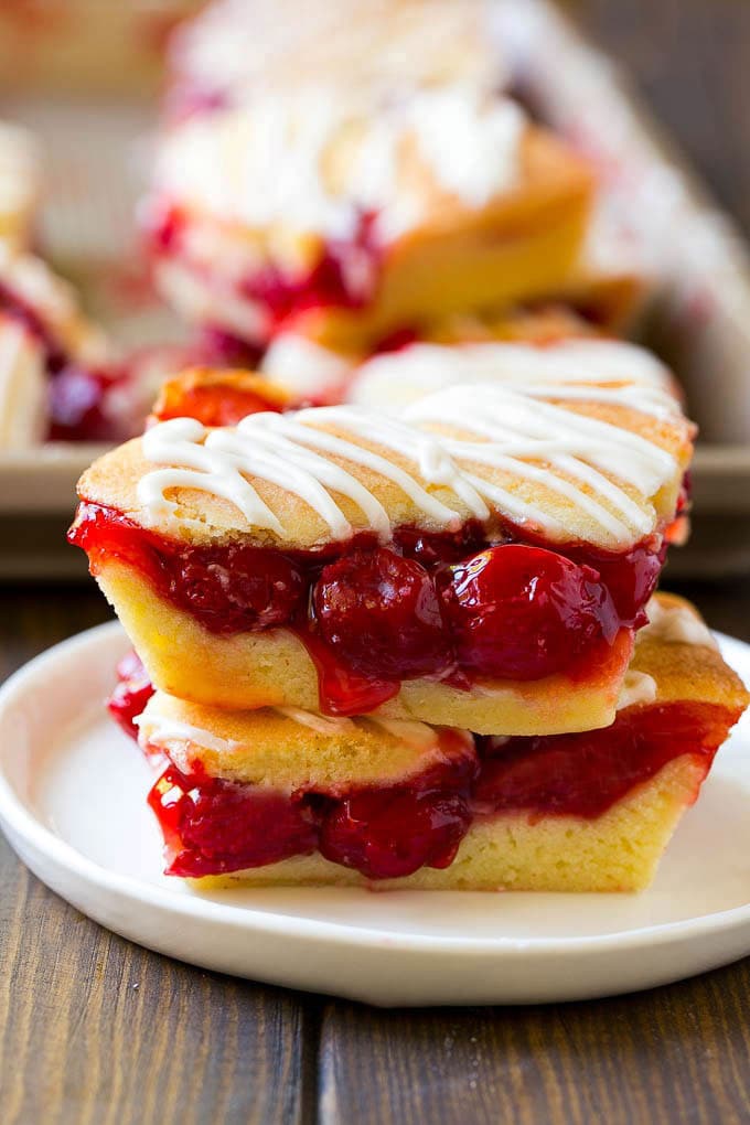 Cherry Bars Recipe | Cherry Pie Bars | Cherry Cookies | Bar Cookies #cookies #bars #cherry #baking #dessert #sweets #sadud Two cherry bars on a plate with a pan of bars in the background.