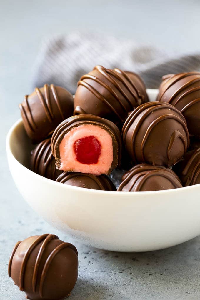 Chocolate Covered Cherries Recipe | Cherry Cordials | Cherry Candy #chocolate #candy #dessert #cherry #sweets #sadud A bowl of chocolate covered cherries with one cut open.