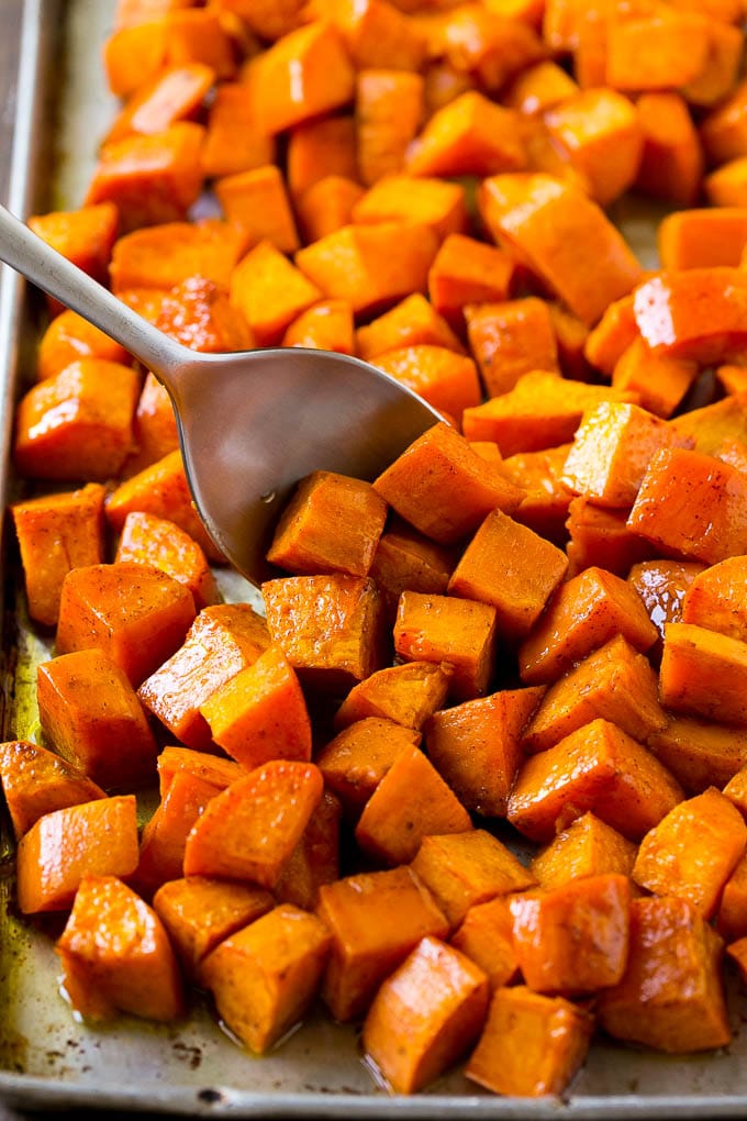 Maple Roasted Sweet Potatoes Recipe | Easy Sweet Potatoes | Baked Sweet Potatoes | Sweet Potato Side Dish #sweetpotatoes #cinnamon #maple #butter #fall #sidedish #dinner #sadud A sheet pan of baked yams flavored with maple and cinnamon, with a serving spoon in them.