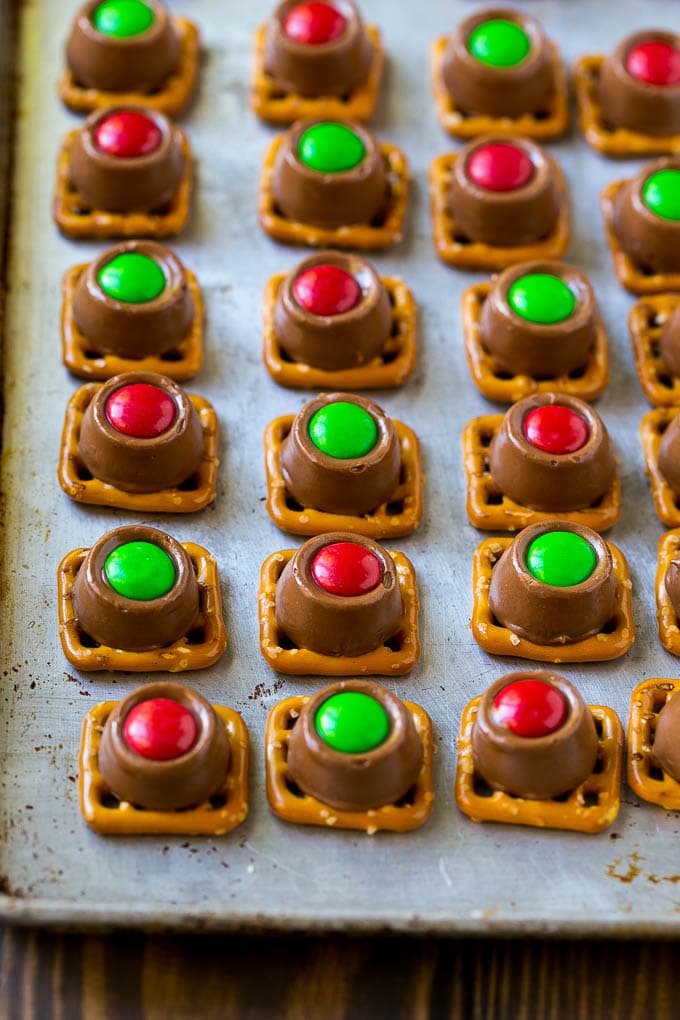Rolo Pretzels Recipe | Chocolate Pretzels | Caramel Pretzels | Holiday Candy #christmas #baking #dessert #candy #chocolate #caramel #pretzels #sadud Treats with red and green M&M's pressed on top all on a baking sheet.