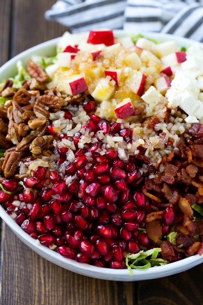 Brussels Sprout Salad Recipe | Shredded Brussels Sprouts Salad | Fall Salad #salad #brusselssprouts #bacon #thanksgiving #pomegranate #apple #dinner #sadud Dressing poured on top of salad that contains sprouts, pomegranate seeds, pecans and bacon.