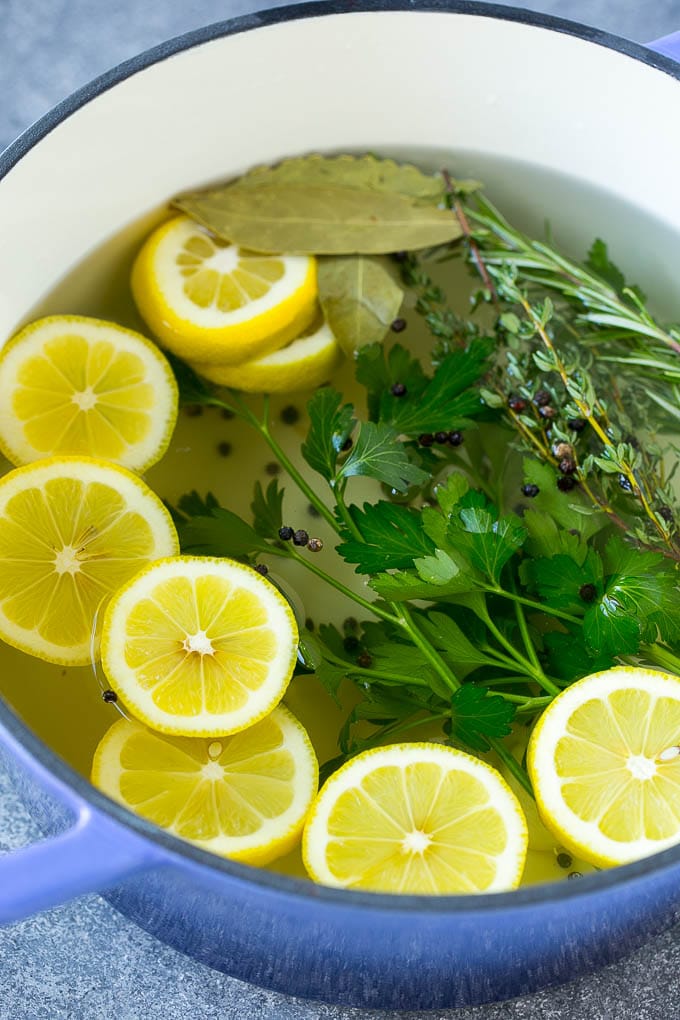 This chicken brine recipe is made with lemons, honey, fresh herbs and spices, and produces a juicy tender chicken every time! A foolproof way for succulent and flavorful roasted, smoked or fried chicken. Salt, water, lemons, herbs and peppercorns in a pot.