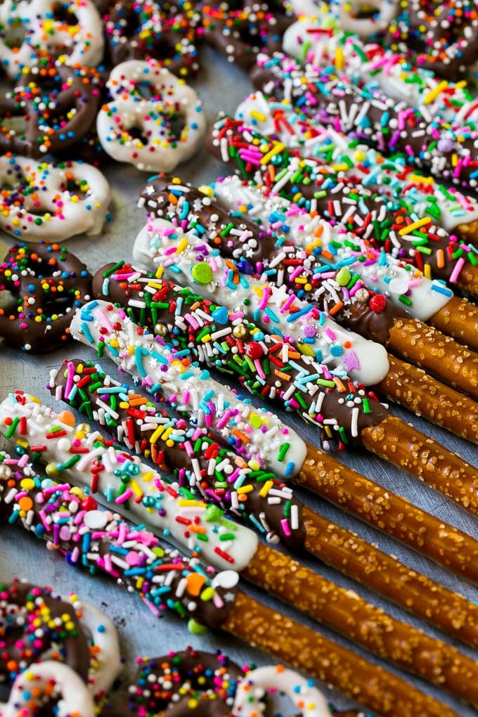 Chocolate Covered Pretzels Recipe | Sprinkle Pretzels | No Bake Dessert #pretzels #chocolate #christmas #sprinkles #candy #sadud A sheet pan with coated twists and rods decorated with rainbow sprinkles.