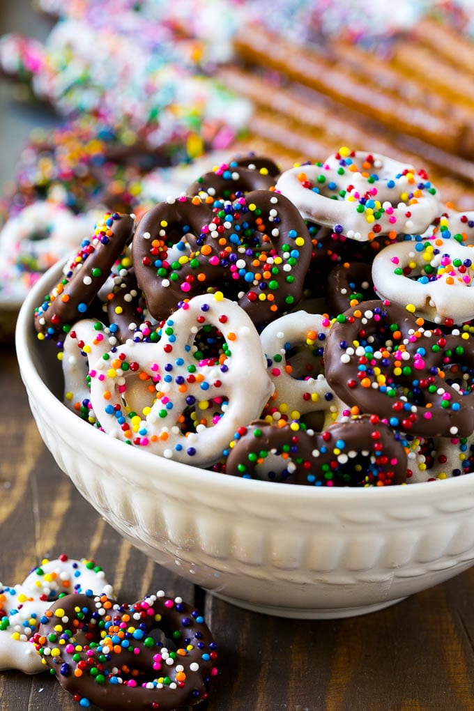 Chocolate Covered Pretzels Recipe | Sprinkle Pretzels | No Bake Dessert #pretzels #chocolate #christmas #sprinkles #candy #sadud A bowl of chocolate covered pretzels decorated with rainbow sprinkles.