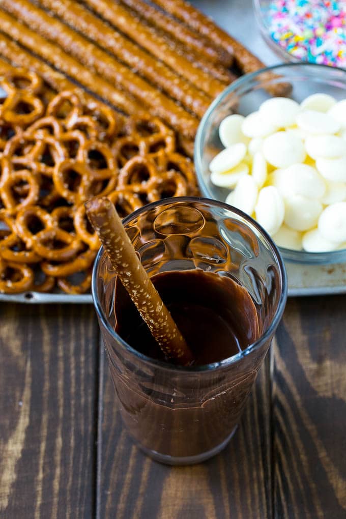 Chocolate Covered Pretzels Recipe | Sprinkle Pretzels | No Bake Dessert #pretzels #chocolate #christmas #sprinkles #candy #sadud A rod in a glass full of melted chocolate.