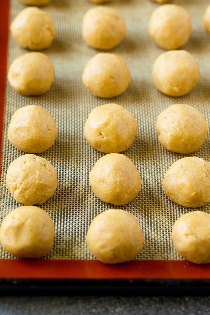 Peanut Butter Blossoms Recipe | Hershey Kiss Cookies | Chocolate Peanut Butter Cookies #cookies #peanutbutter #chocolate #dessert #baking #christmas #christmascookies #sadud Balls of dough on a baking sheet.