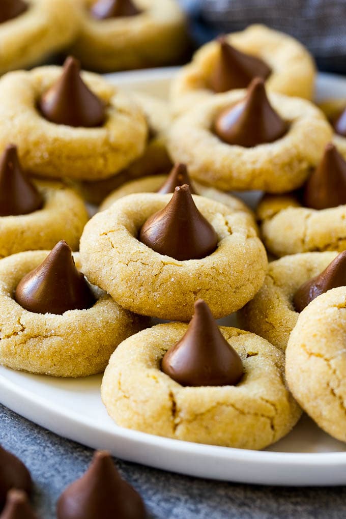 Peanut Butter Blossoms Recipe | Hershey Kiss Cookies | Chocolate Peanut Butter Cookies #cookies #peanutbutter #chocolate #dessert #baking #christmas #christmascookies #sadud A plate with peanut butter blossoms stacked onto it.