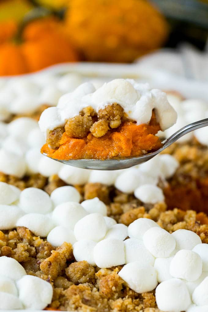 This recipe for sweet potato casserole with marshmallows is mashed spiced sweet potatoes, topped with both a pecan streusel topping and plenty of mini marshmallows. A holiday classic that's a family favorite! A serving spoon holding up a portion of sweet potato casserole with marshmallows.