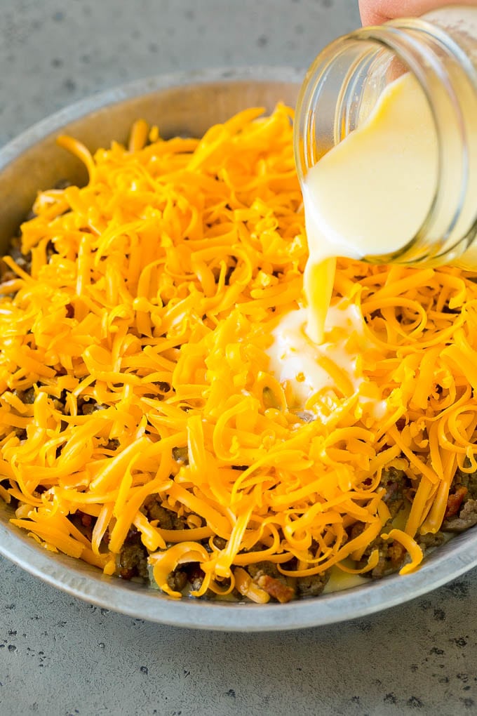 Cheeseburger Pie Recipe | Cheeseburger Casserole | Ground Beef Recipe #cheeseburger #beef #bacon #cheese #casserole #dinner #sadud Egg batter being poured over shredded cheese and ground beef.